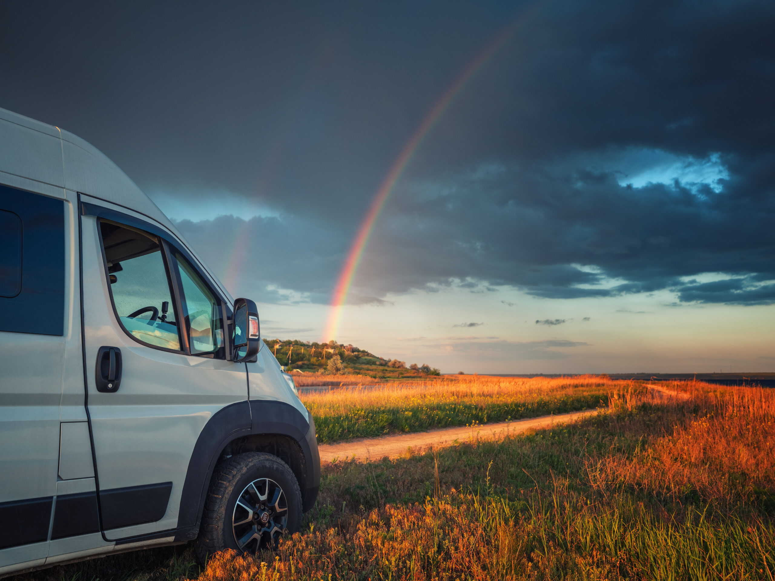 Camper van parked near a rainbow at golden hour